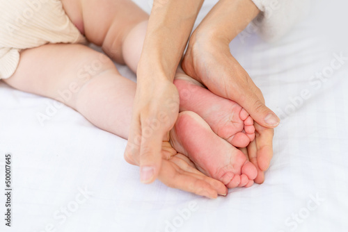mom's hands hold the baby's legs on a white bed