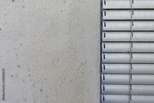 Detal architektoniczny na fragment elewacji domu jednorodzinnego wykonanego z betonu. Widoczny fragment żaluzji aluminiowych elewacyjnych.