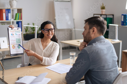 Happy young businesswoman showing chart, presenting financial report to her boss or colleague at modern office