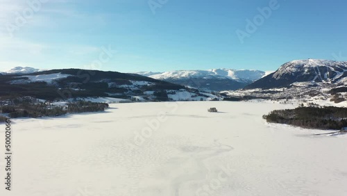 Reverse aerial over frozen massive lake Tunhovdfjorden in Norway with mountain Dyna and Myking in background photo