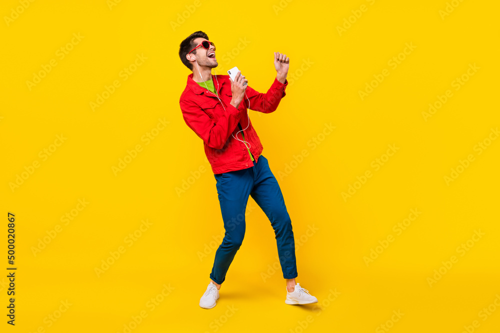Full body photo of crazy young guy dance listen music sing wear glasses jacket jeans shoes isolated on yellow background