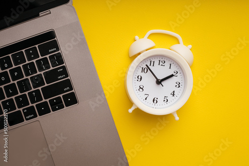 Top view of laptop and alarm clock on yellow background. Deadline and urgent tasks concept
