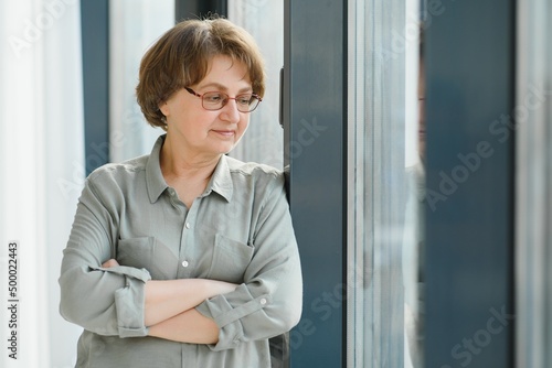 Free Download Portrait of beautiful senior woman. Elderly lady is standing by window at home. Active longevity concepts - GFXLoad