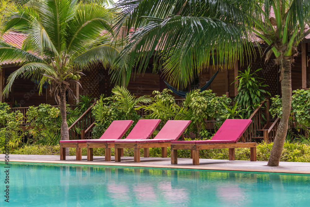 Swimming pool with relaxing beds and green palm trees in tropical garden , Thailand