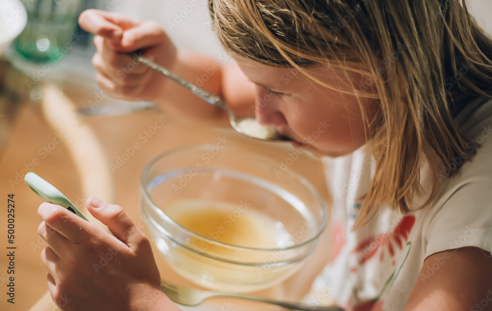 Teenage girl eating breakfast and looking at the smartphone Teenage girl eating breakfast and looking at the smartphone