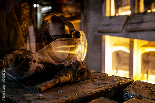 A protective mask and gloves lie on zinc ingots against the background of blurred burning blast furnaces, metal smelters. Industrial furnaces for zinc smelting. Factory. Work. Production. photo