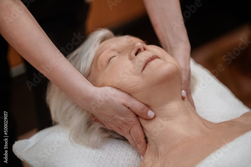 A gray-haired woman looking relaxed while having face massage