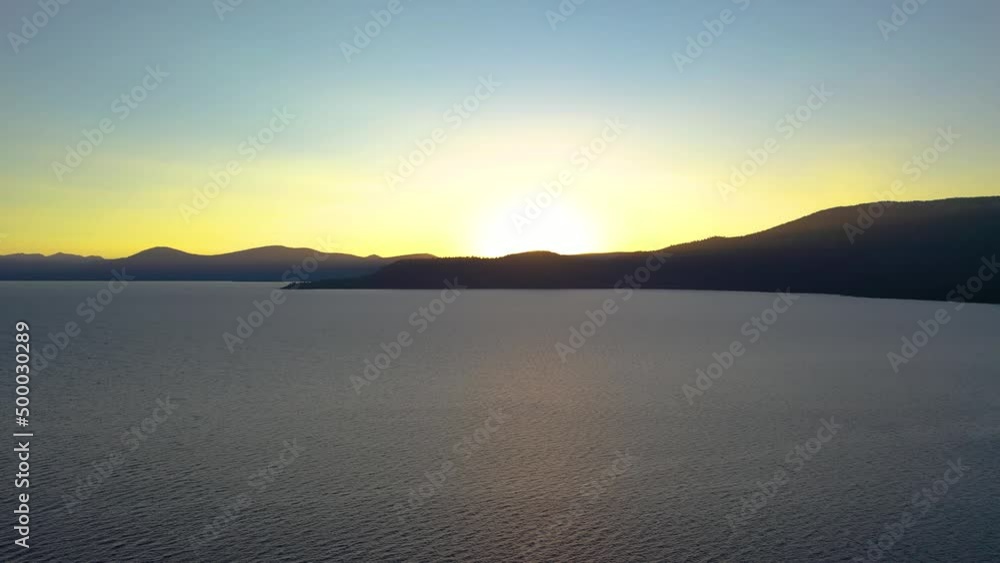 Alaskan Sunrise on Lake Clark with Beautiful Water and Mountain Silhouette in the Background. National Park Recreation Area. Bright Orange Sun with Golden Glow. Aerial Drone View Alaskan Sunrise on Lake Clark with Beautiful Water and Mountain Silhouette in the Background. National Park Recreation Area. Bright Orange Sun with Golden Glow. Aerial Drone View
