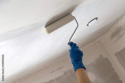 A worker applying whitewash on the ceiling using a handle roller at home
