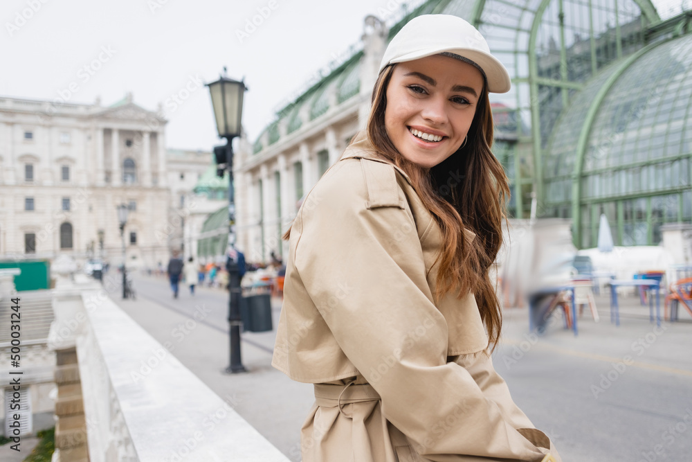 happy young woman in stylish trench coat and baseball cap.
