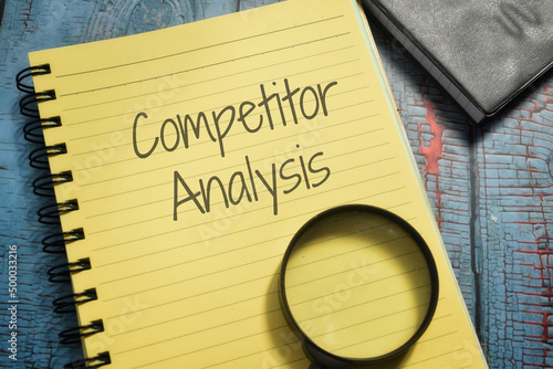 Closeup shot of a yellow notebook page with a magnifying glass and the writing competitor analysis photo
