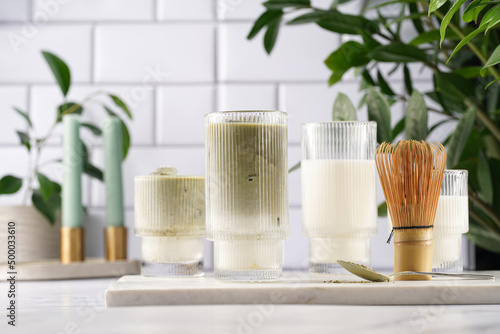 tall rippled glass with matcha latte - japanese green tea powder and whipped milk on marble board in white kitchen