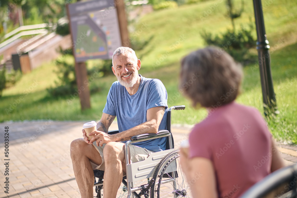 A man in a wheel chair and a woman havinng coffee in the park A man in a wheel chair and a woman havinng coffee in the park