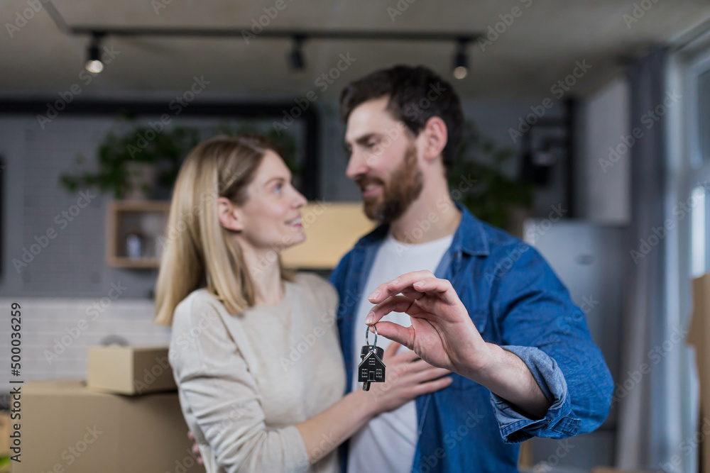 Selected focus, married couple man and woman happy together, hugging, holding the keys to their new apartment, housewarming, close-up photo Selected focus, married couple man and woman happy together, hugging, holding the keys to their new apartment, housewarming, close-up photo