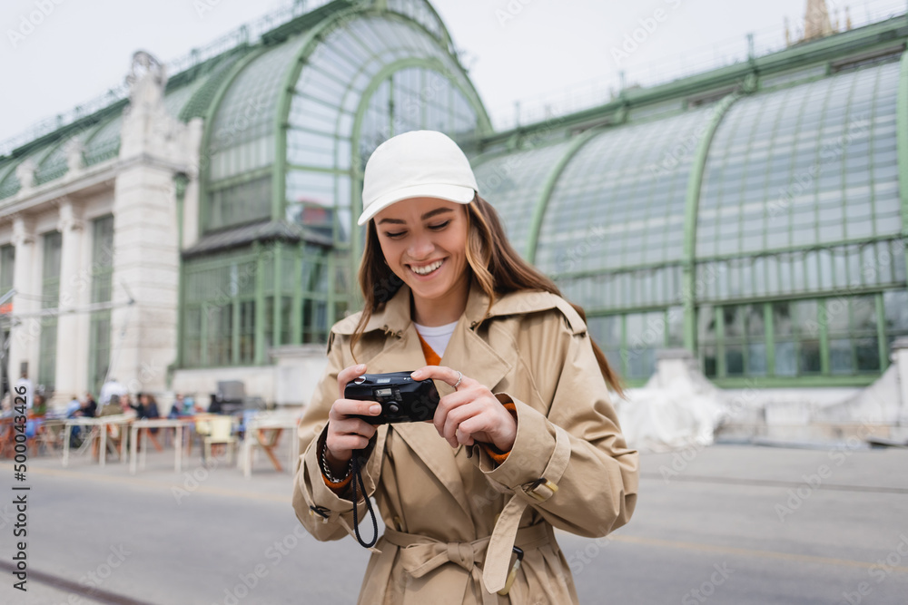 happy young woman in beige trench coat and baseball cap holding vintage camera.