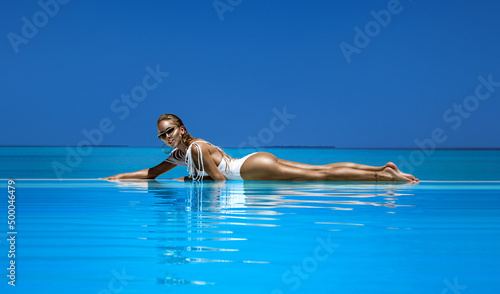 Elegant woman in white swimsuit in pool on tropical Maldives island. Beautiful bikini body girl in pool with view on horizon. Elegant model near the pool on beautiful Indian ocean landscape. Travel © marcink3333