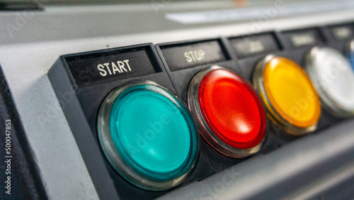 Close up view of the start push button on the industrial control panel of a electrical machine. There are start, stop, jog, enable, comm. and emergency stop buttons.