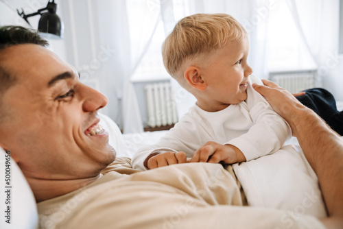 White man playing with his son while lying on bed together
