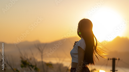 Fotografiet Young girl standing outdoors and looking at the mountains against dusk sky at su