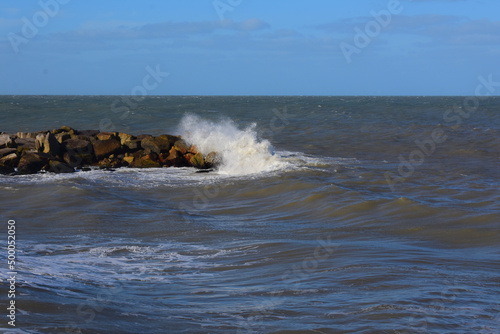 Beautiufl shot of a wavy sea crashing stones in a beach under a blue sky on a sunny day photo