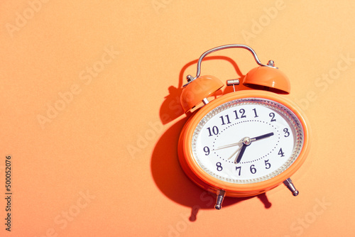 Orange retro style alarm clock on orange background under the bright sunlight,