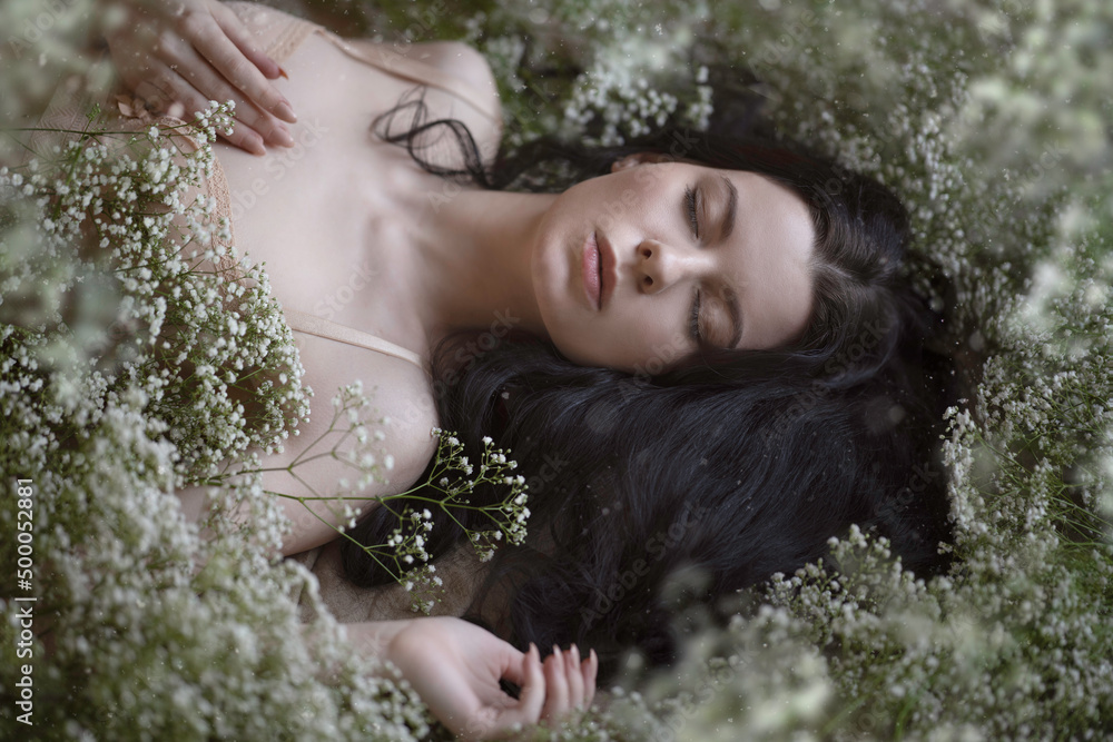 Tender dark-haired girl lies on gypsophila flowers Tender dark-haired girl lies on gypsophila flowers