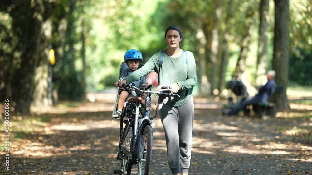 Happy mother and child outside carrying bike toddler in bicycle back seat Happy mother and child outside carrying bike toddler in bicycle back seat