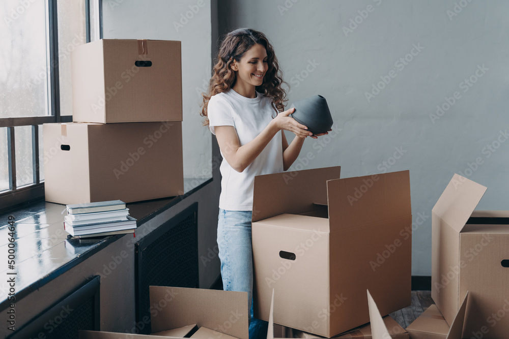 Happy girl unpacking cardboard boxes and taking the vase. European woman packing boxes to move. Happy girl unpacking cardboard boxes and taking the vase. European woman packing boxes to move.
