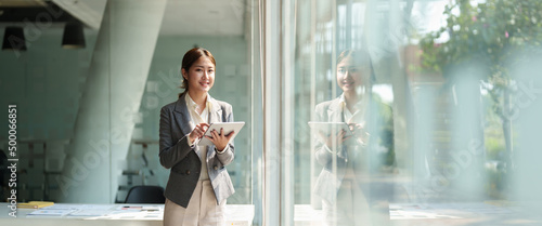 attractive business asian woman standing near window and using smart digital tablet.