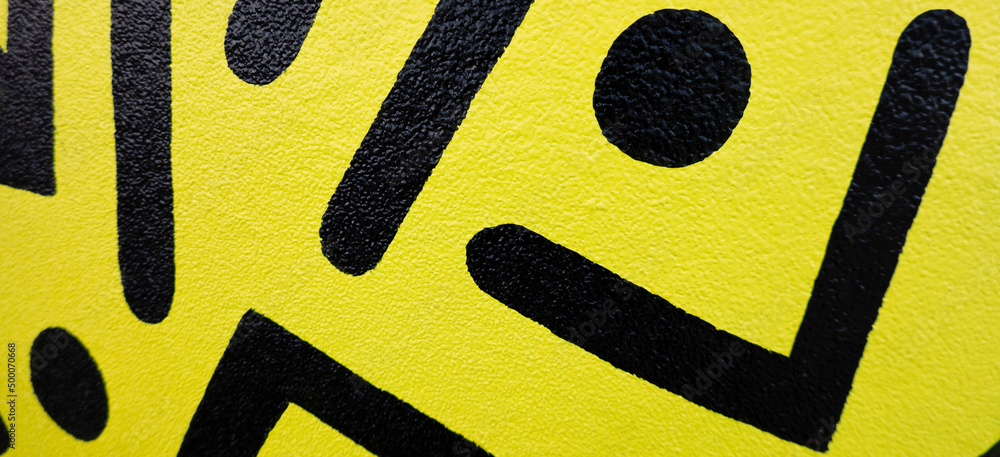 Naklejka premium Fragment of the yellow painted wall with geometric black colors graffiti painting in the street. Part of colorful street art graffiti on wall background