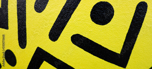 Fragment of the yellow painted wall with geometric black colors graffiti painting in the street. Part of colorful street art graffiti on wall background