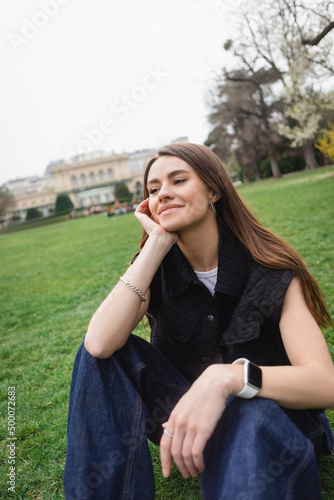 pleased young woman in sleeveless jacket sitting on lawn.