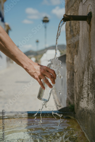 vertical photo of a hand holding a glass bottle while water overflows from the bottle. Water falls from a natural spring water source.