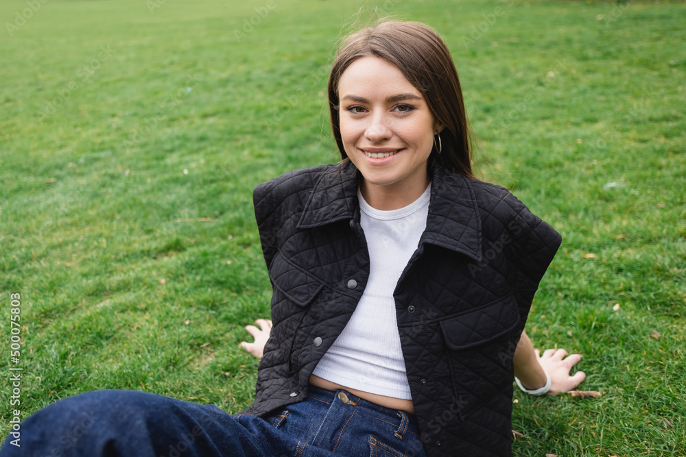 smiling young woman in sleeveless jacket sitting on lawn. smiling young woman in sleeveless jacket sitting on lawn.