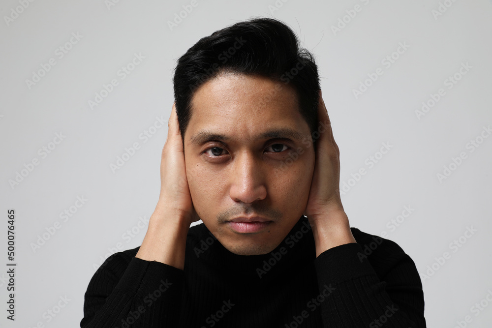 Asian man is covering his ears and looking at the camera. Mental health issues. Asian man is covering his ears and looking at the camera. Mental health issues.