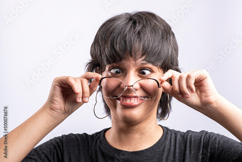 Latina woman holding her glasses while making funny faces on a white background