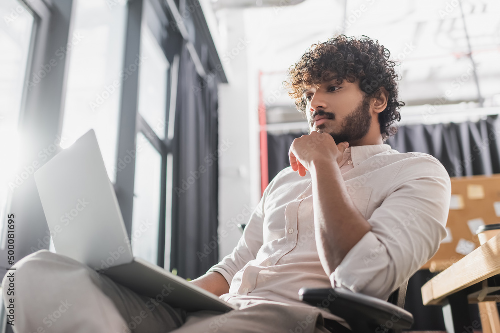 Low angle view of young indian businessman using blurred laptop in office. Low angle view of young indian businessman using blurred laptop in office.