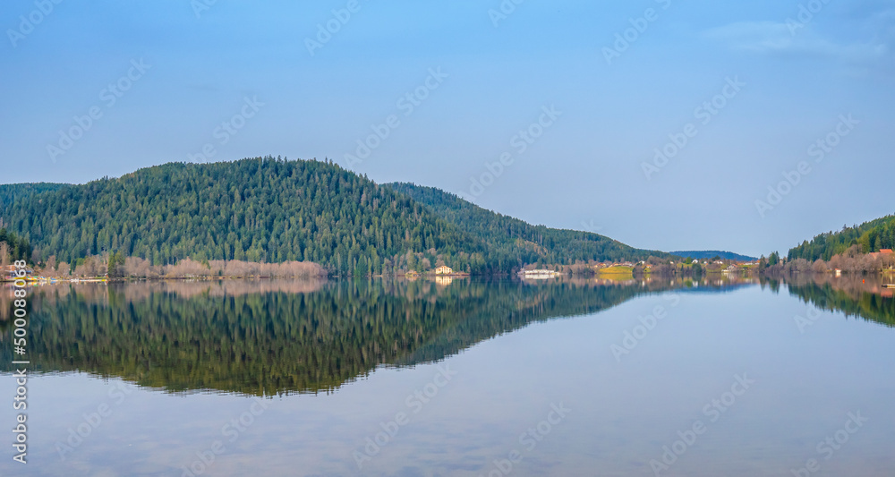 Lac de Gérardmer dans les Vosges, un matin de printemps. Reflets dans un lac miroir sous un ciel bleu et le regard des montagnes vosgiennes.