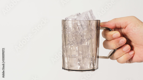 Hand is holding a plastic gloass with ice cubes on white background.. photo