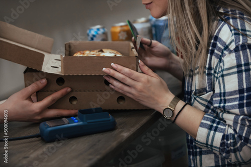 a young woman buys ready-made food in cardboard boxes, on pre-order and pays with a card through a bank terminal