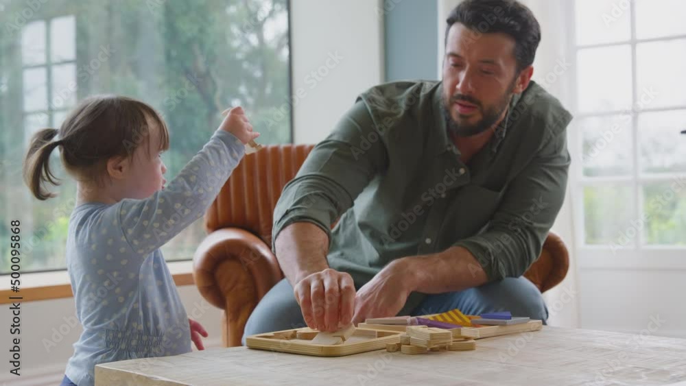 Down syndrome girl playing game with father sorting wooden letter shapes at home together - shot in slow motion Down syndrome girl playing game with father sorting wooden letter shapes at home together - shot in slow motion