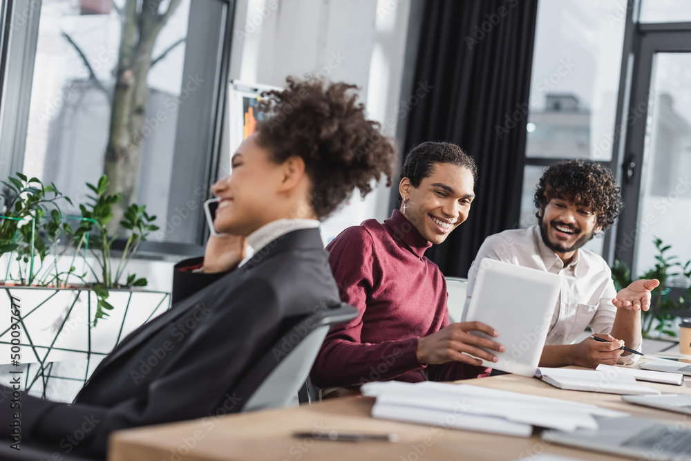 Cheerful multiethnic businessmen using digital tablet while african american colleague talking on smartphone in office. Cheerful multiethnic businessmen using digital tablet while african american colleague talking on smartphone in office.