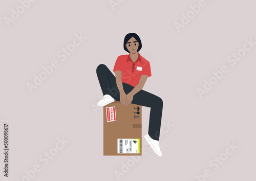 A young female Caucasian courier sitting on a parcel with stickers, delivery service