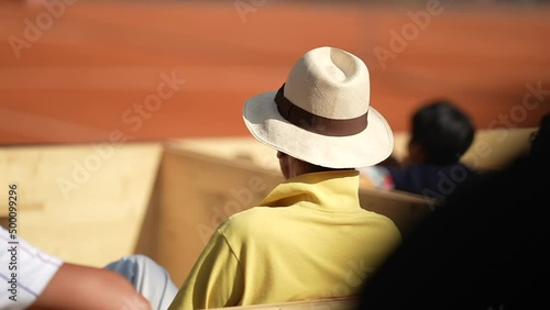 Person wearing panama hat sitting audience seat watching sport game outside photo