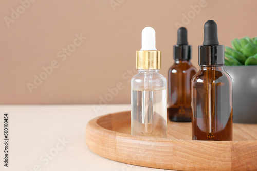 Glass bottles on wooden plate. Natural skin care SPA beauty product design. Mineral organic oil cosmetics on beige background. Earth tones. Mock-Up. Oily pipette. Face and body treatment. Front View