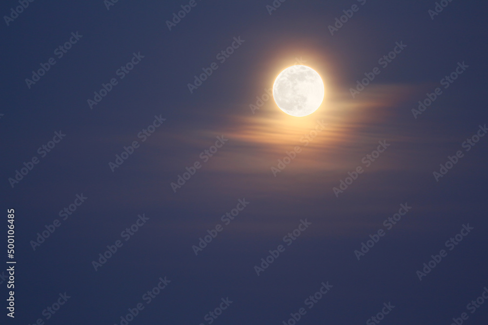 Color photograph of a large moon in the evening sky with beautiful clouds and gentle light. Bright light on a full moon.