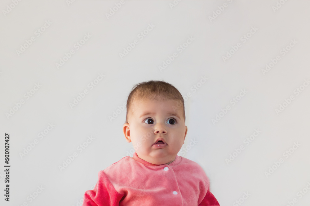 discouraged baby in pink clothes looks up in surprise. big eyes, 9 months discouraged baby in pink clothes looks up in surprise. big eyes, 9 months