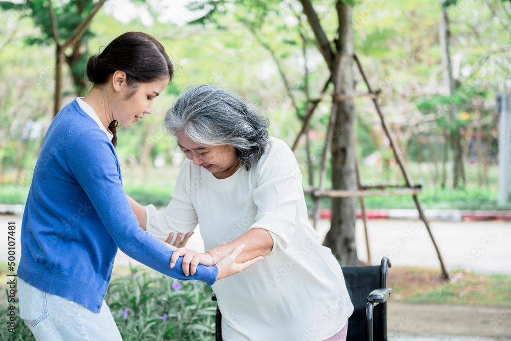 Obraz premium Asian family, attractive young daughter helping her mother to get up from the wheelchair to do physical therapy with learning to walk, to Asian family and osteoarthritis concept.
