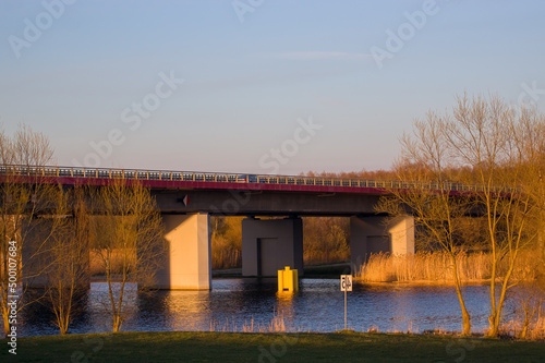 Pięknie oświetlony most nad rzeką w otoczeniu żółtych traw