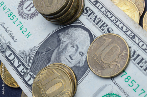 The American dollar on top of which lie Russian coins with a face value of 10 rubles. Translation of the inscriptions on the coins: "10 rubles". close-up